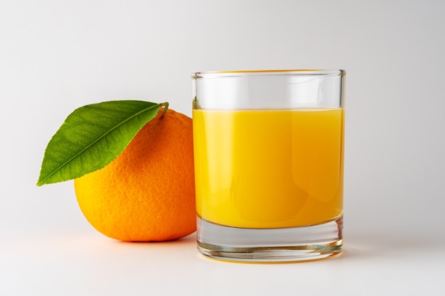 Copo de suco de laranja e fruta laranja em fundo branco.