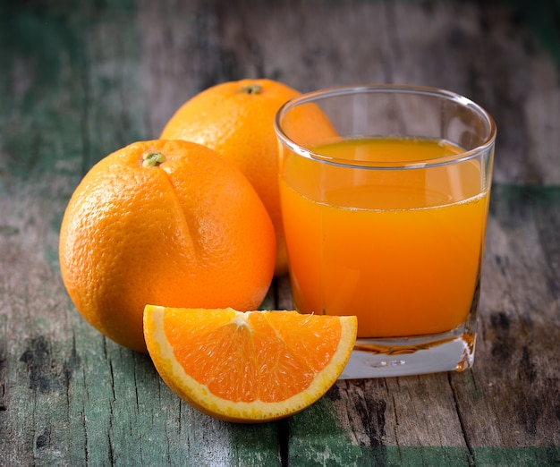 Copo de suco de laranja e laranjas frescas na madeira