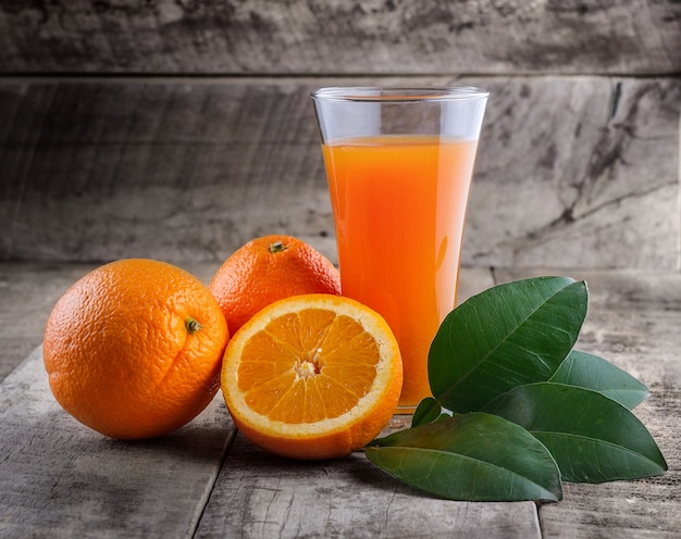 Copo de suco de laranja e laranjas frescas na madeira