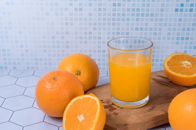 Copo de suco de laranja espremido sobre uma tábua e laranjas ao redor