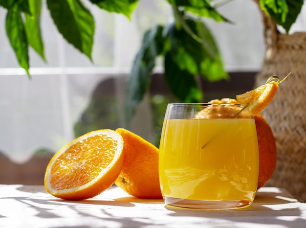 Copo de suco de laranja fresco com laranjas maduras na mesa de madeira branca no terraço de verão