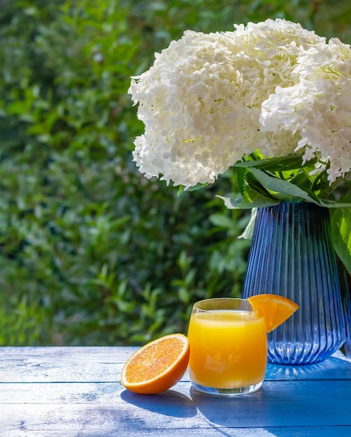 Copo de suco de laranja fresco decorado com uma fatia de laranja madura na mesa de madeira azul com flores no fundo