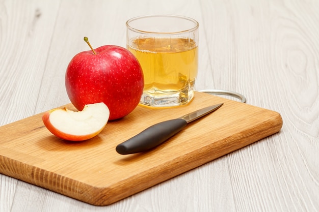 Copo de suco de maçã com maçã vermelha e faca na tábua de madeira com fundo cinza