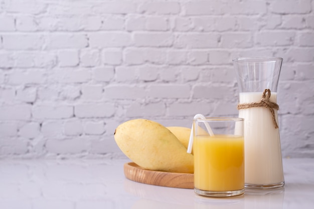 Foto copo de suco de manga e jarro de leite na mesa.