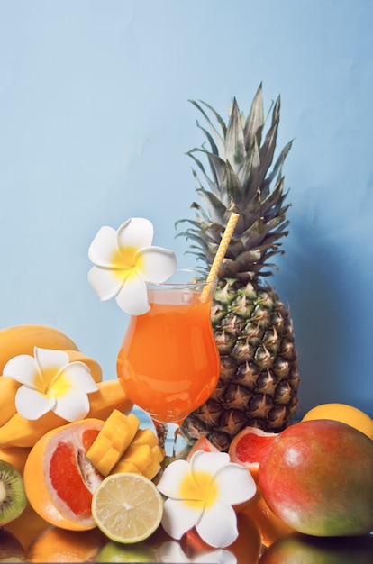 Copo de suco de multifrutas exóticas tropicais cocktail com flores de frangipani e frutas no fundo