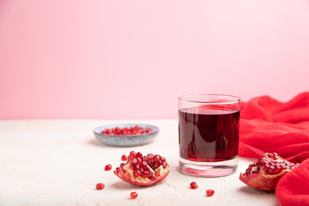 Copo de suco de romã em um fundo branco e rosa com tecido vermelho.