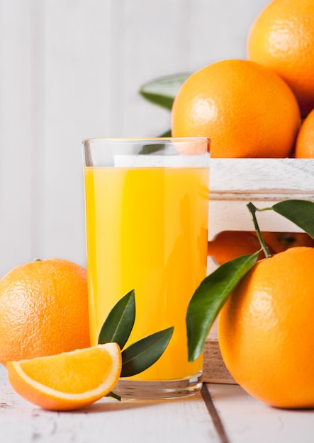 Copo de suco de suco de laranja orgânico fresco com laranjas cruas em caixa de madeira branca