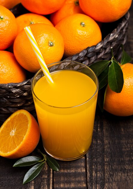 Copo de suco de suco de laranja orgânico fresco com laranjas cruas no fundo escuro de madeira