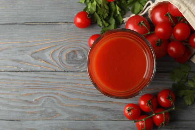 Foto copo de suco de tomate e tomate na mesa de madeira cinza