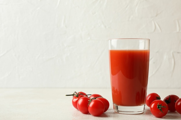 Copo de suco de tomate e tomates em fundo branco texturizado