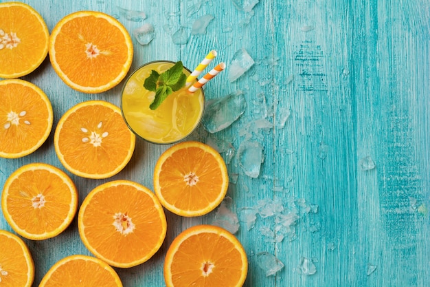 Copo de suco, folhas de hortelã, gelo e fatias de laranja planas sobre madeira rústica azul