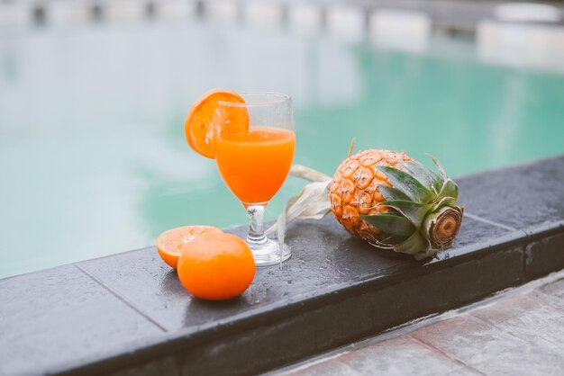 Copo de suco na beira da piscina suco de laranja com laranja e abacaxi na piscina