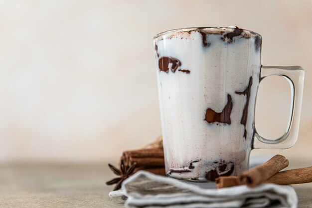 Copo de vidro com bebida de chocolate quente ou cacau e paus de canela com erva-doce