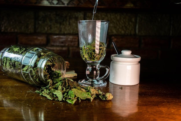 Copo de vidro e pote com folhas secas para infusão na mesa de madeira
