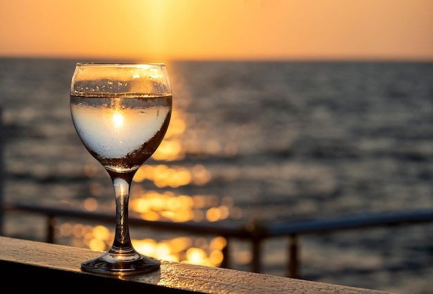 Copo de vinho branco ao pôr do sol perto do mar com espaço de cópia