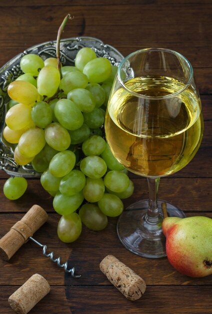 Copo de vinho branco, cacho de uvas suculentas, pêra e saca-rolhas na mesa de madeira. Vista do topo. Ã Â¡lose-up.