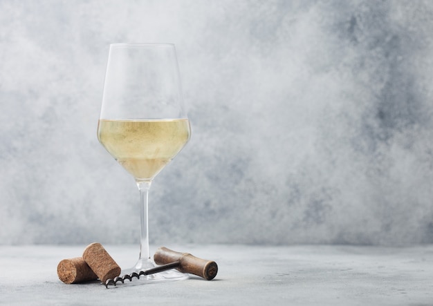 Foto copo de vinho branco de verão com rolhas e saca-rolhas no fundo da mesa de luz.