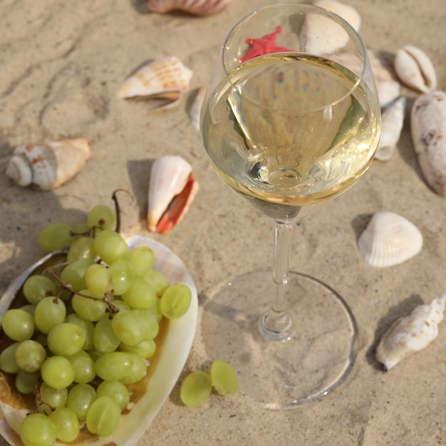 copo de vinho branco na areia como fundo com conchas