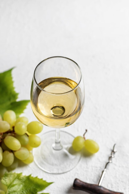 Copo de vinho branco sobre fundo branco com espaço de texto saca-rolhas e uvas