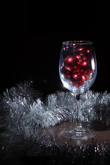 Copo de vinho cheio de bolas de Natal. Sobre um fundo preto.