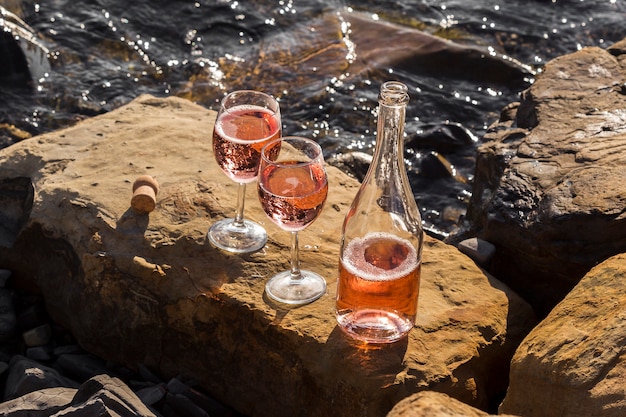 Copo de vinho de alta vista e garrafa nas rochas do oceano