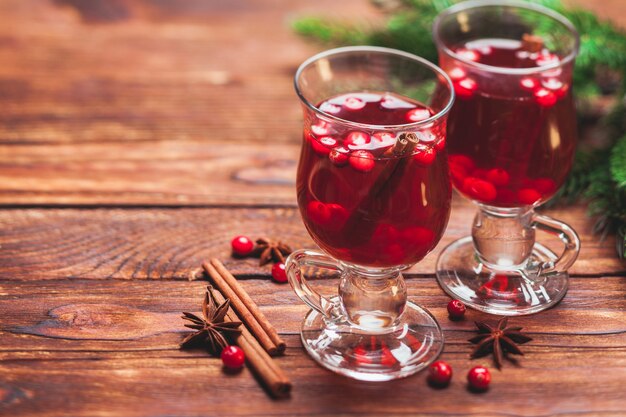 Copo de vinho quente com cranberry e paus de canela perfumados em uma mesa de madeira