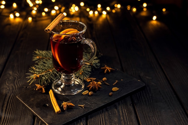 copo de vinho quente com laranja e canela em fundo preto escuro