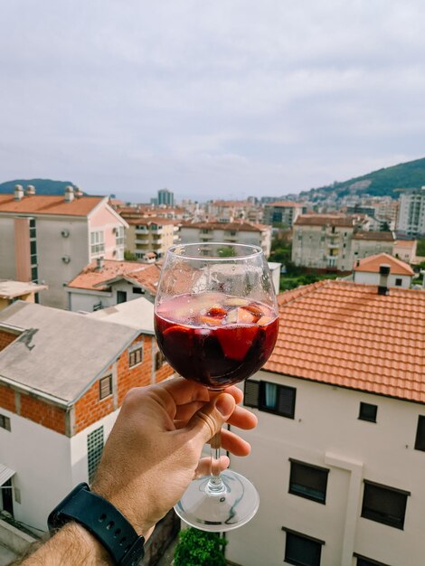 Copo de vinho quente na mão de um homem contra o fundo de telhados vermelhos de casas