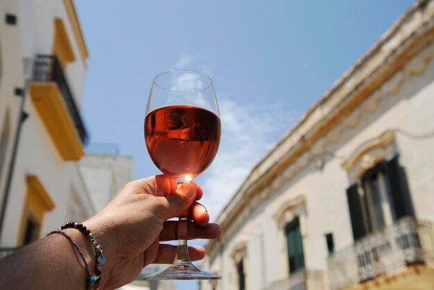 Copo de vinho rosé na mão do homem contra um fundo de céu azul Closeup conceito de humor relaxado na histórica cidade italiana