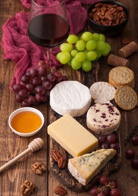 Copo de vinho tinto com seleção de vários queijos na placa e uvas no fundo da mesa de madeira. blue stilton, red leicester e queijo brie e mel.
