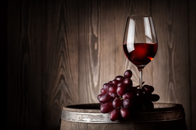 Copo de vinho tinto com uvas no barril de madeira