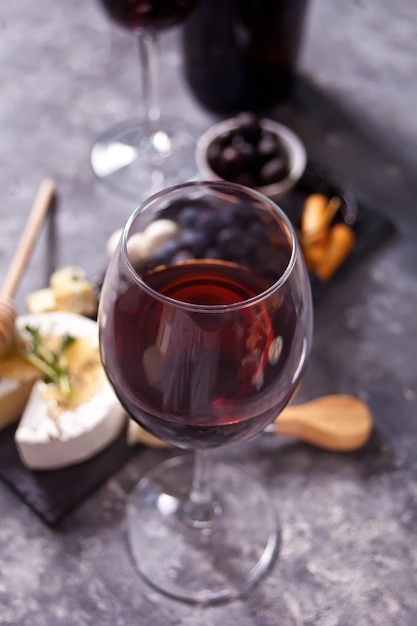 Copo de vinho tinto e prato com queijo variado, frutas e outros petiscos para festa