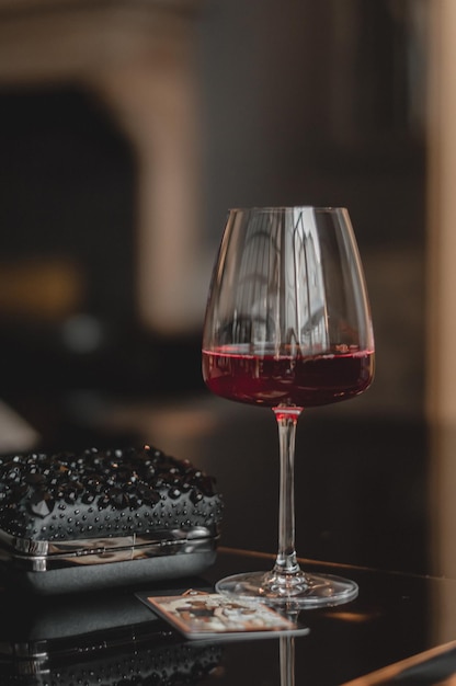 Copo de vinho tinto fica em uma mesa escura ao lado da bolsa de uma mulher lindos copos para bebidas café