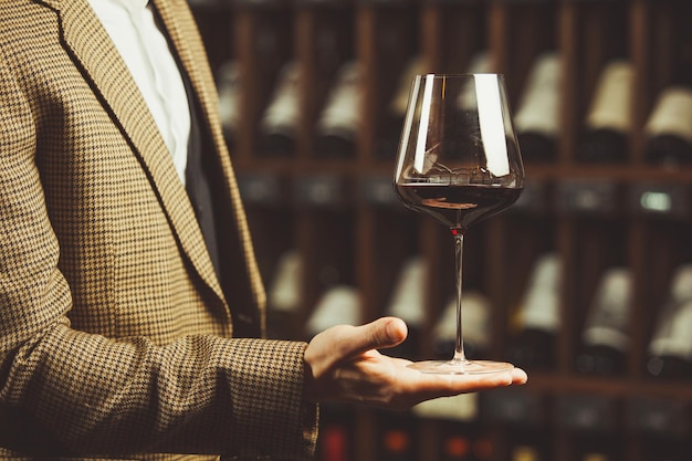 Copo de vinho tinto na mão do sommelier na adega com fundos de garrafas