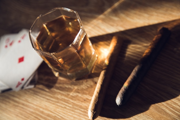 Copo de whisky, charuto e cartas na mesa