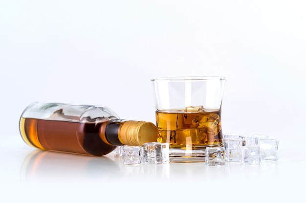 Copo de whisky com cubos de gelo e garrafa no fundo branco