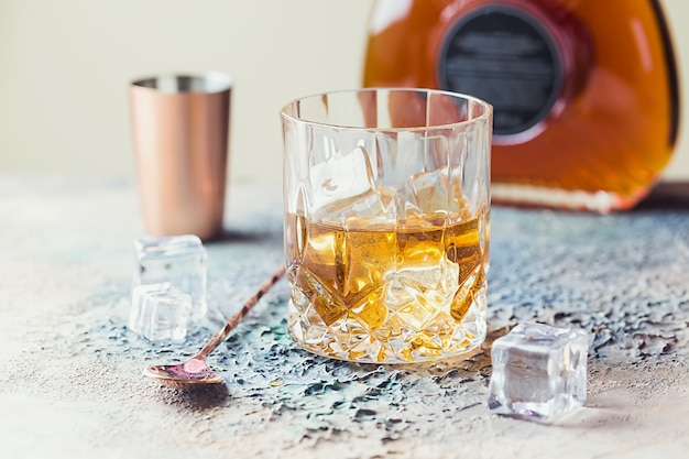 Copo de whisky escocês com cubos de gelo, garrafa e acessórios de barra de cobre