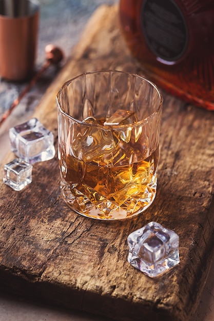 Copo de whisky escocês com cubos de gelo, garrafa e acessórios de barra de cobre