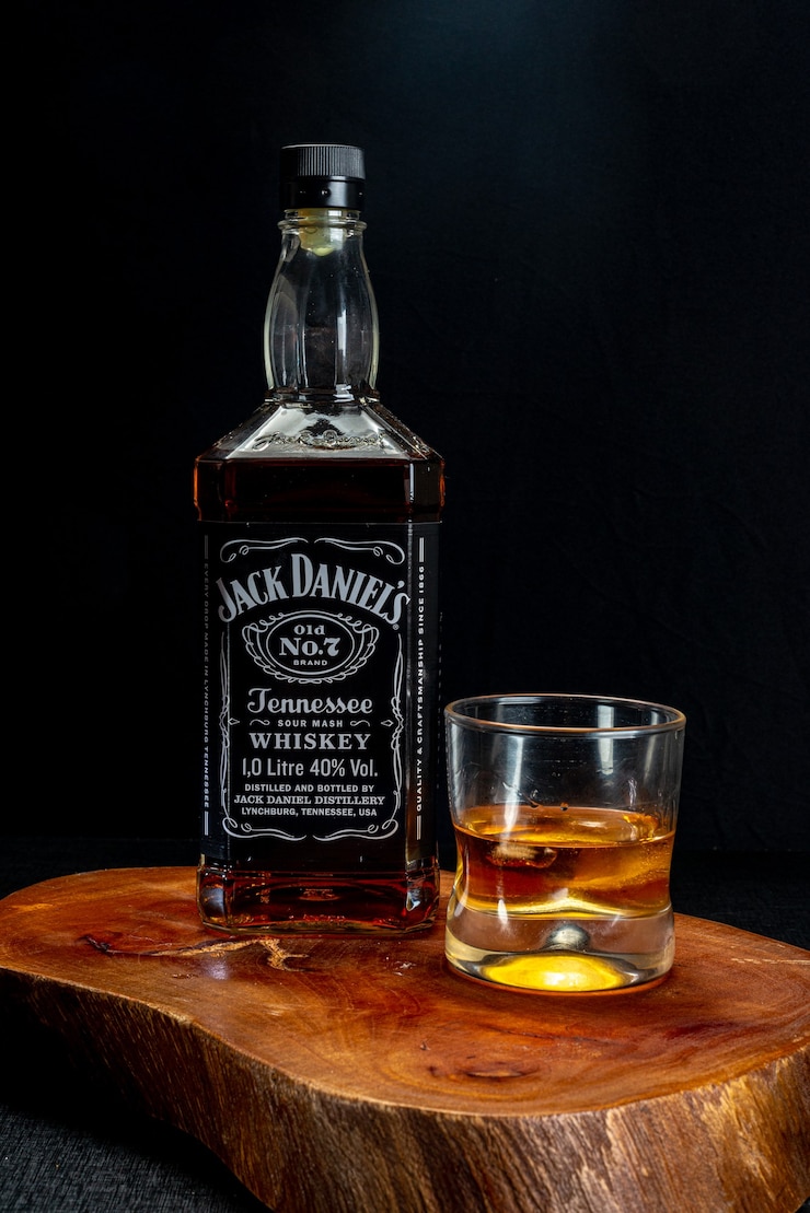 Foto copo de whisky servido com gelo e garrafa de jack daniels em madeira rústica sobre fundo preto