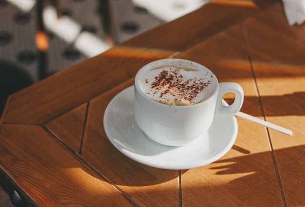 Copo do café do cappuccino com espuma e canela em uma tabela de madeira.