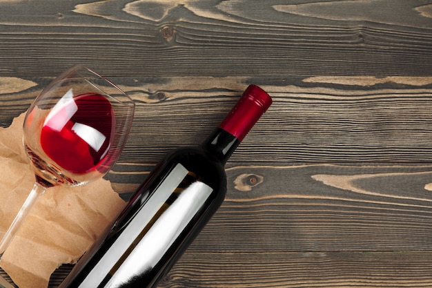 Foto copo e garrafa com vinho tinto no fundo de madeira, vista superior