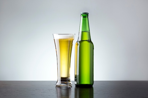 Copo e garrafa de cerveja fresca em fundo cinza