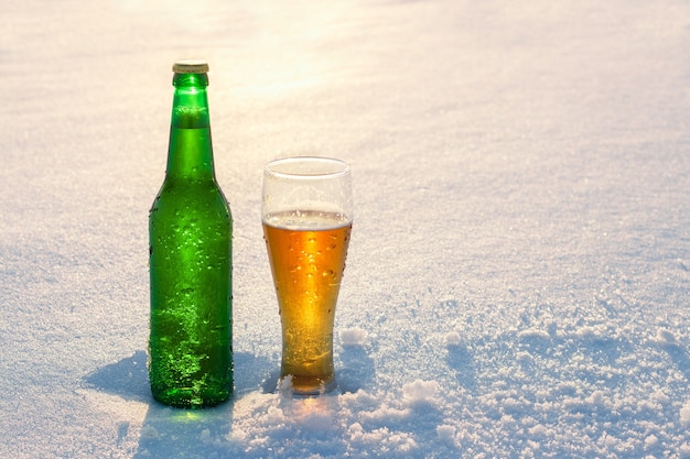 Copo e garrafa de cerveja gelada na neve ao pôr do sol lindo fundo de inverno recreação ao ar livre publicidade de bebida alcoólica bebida alcoólica e feriados