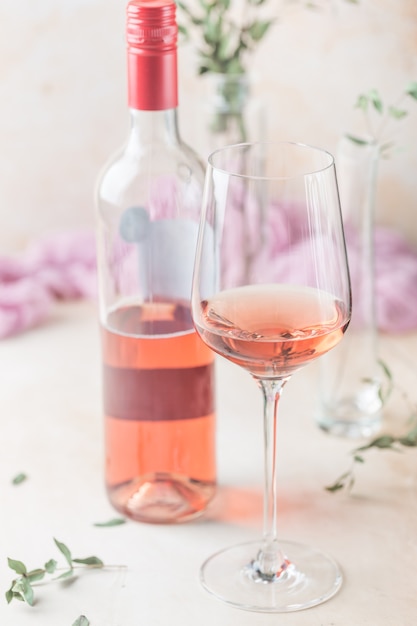 Copo e garrafa de vinho rosé sobre fundo claro.