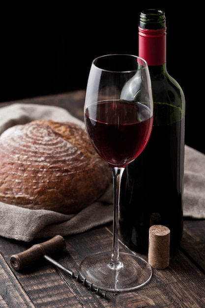 Copo e garrafa de vinho tinto com pão fresco com saca-rolhas retrô na cozinha na mesa de madeira