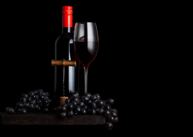 Copo e garrafa de vinho tinto com uvas escuras e saca-rolhas vintage