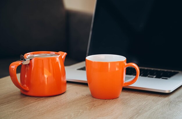 Foto copo laranja e bule no fundo de um laptop no local de trabalho