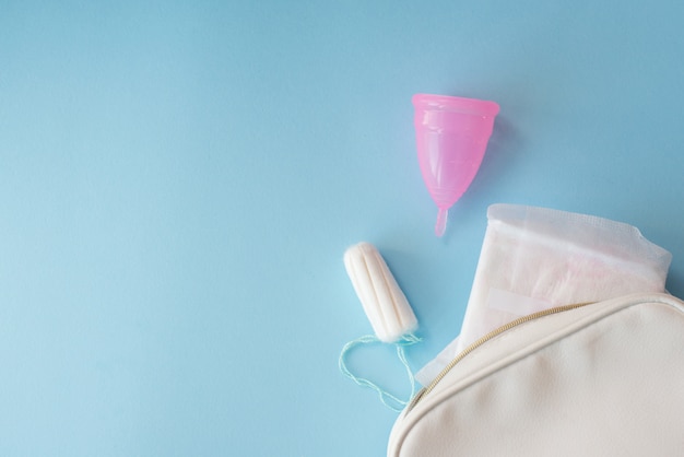 Copo menstrual, almofadas e tampão com bolsa branca sobre fundo azul