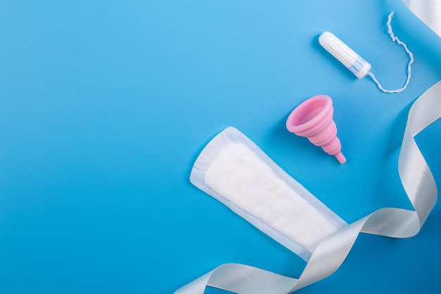 Copo menstrual amarelo de silicone com almofadas e tampões de higiene alternativa em um plano de fundo rosa