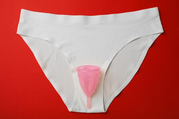 Copo menstrual e calcinha na vista superior de fundo vermelho
